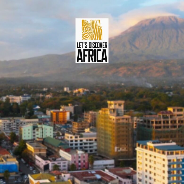 Logo reading 'Let's Discover Africa' with zebra illustration on white card over a blurred city and mountain backdrop.